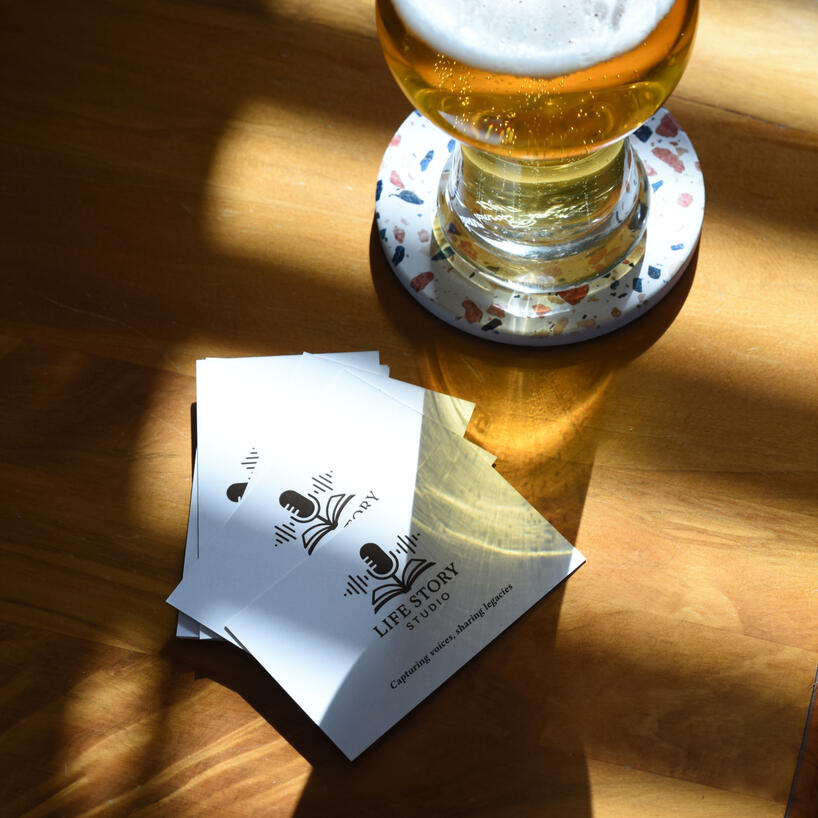 life-story-studio-business-cards.jpg Life Story Studio business cards sat on a table next to a glass of beer.